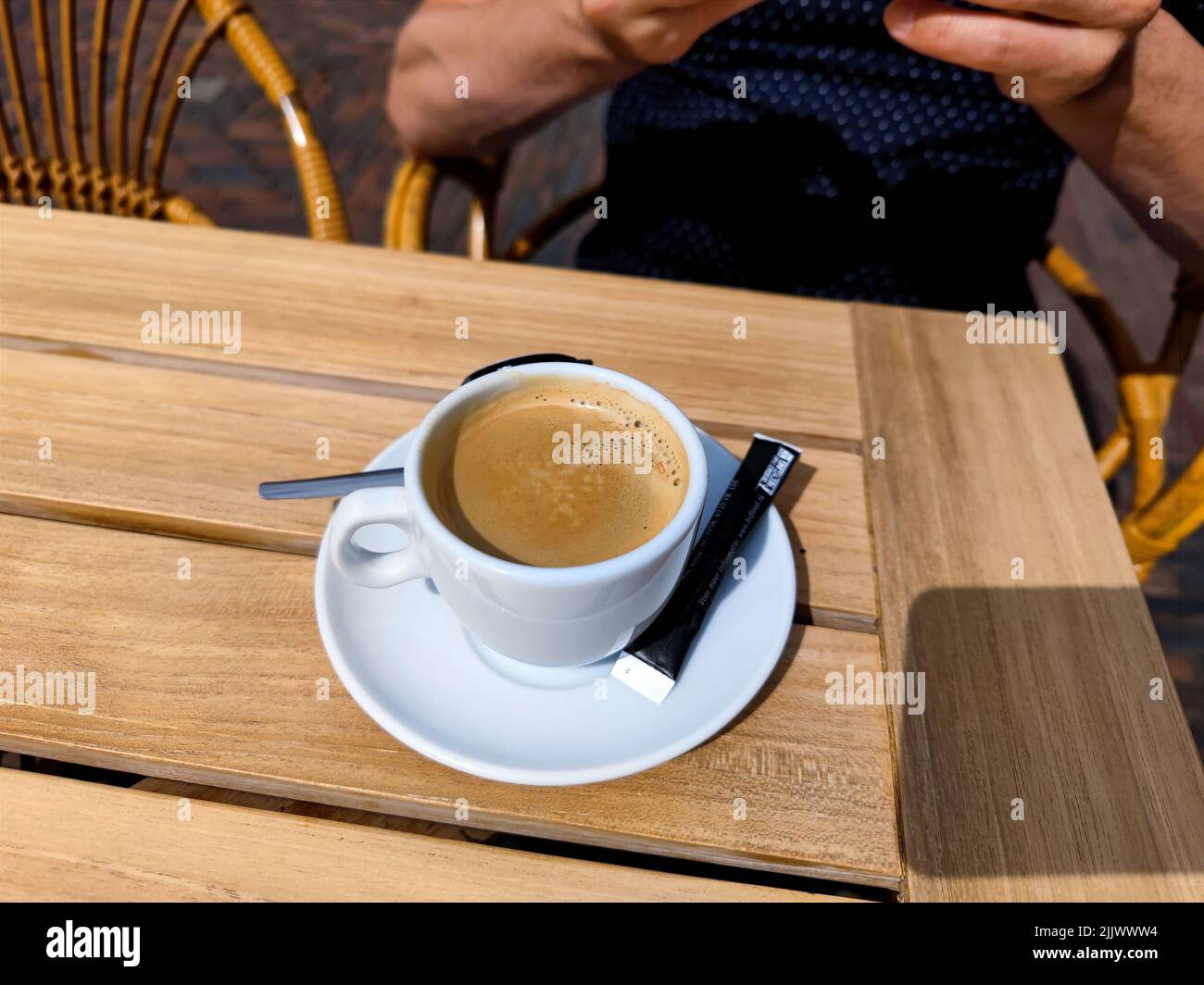 Tazza di caffè appena preparata con un sacchetto di zucchero, una tazza di latte di caffè e un cucchiaio su un tavolo in legno da terrazza. Non ci sono persone o marchi negli Foto Stock
