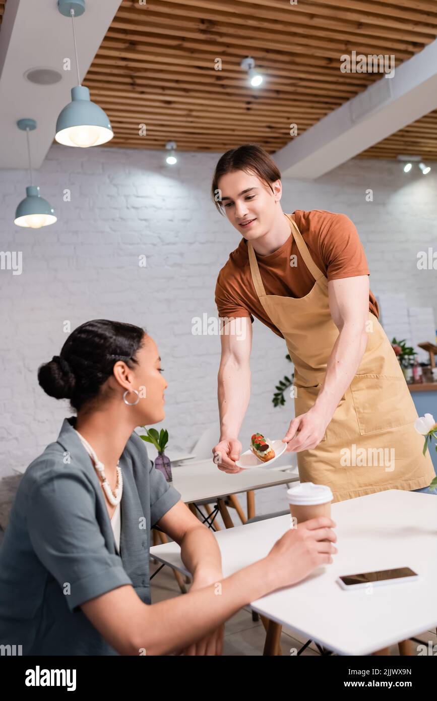 Un venditore sorridente che dà dessert al cliente afro-americano in pasticceria Foto Stock