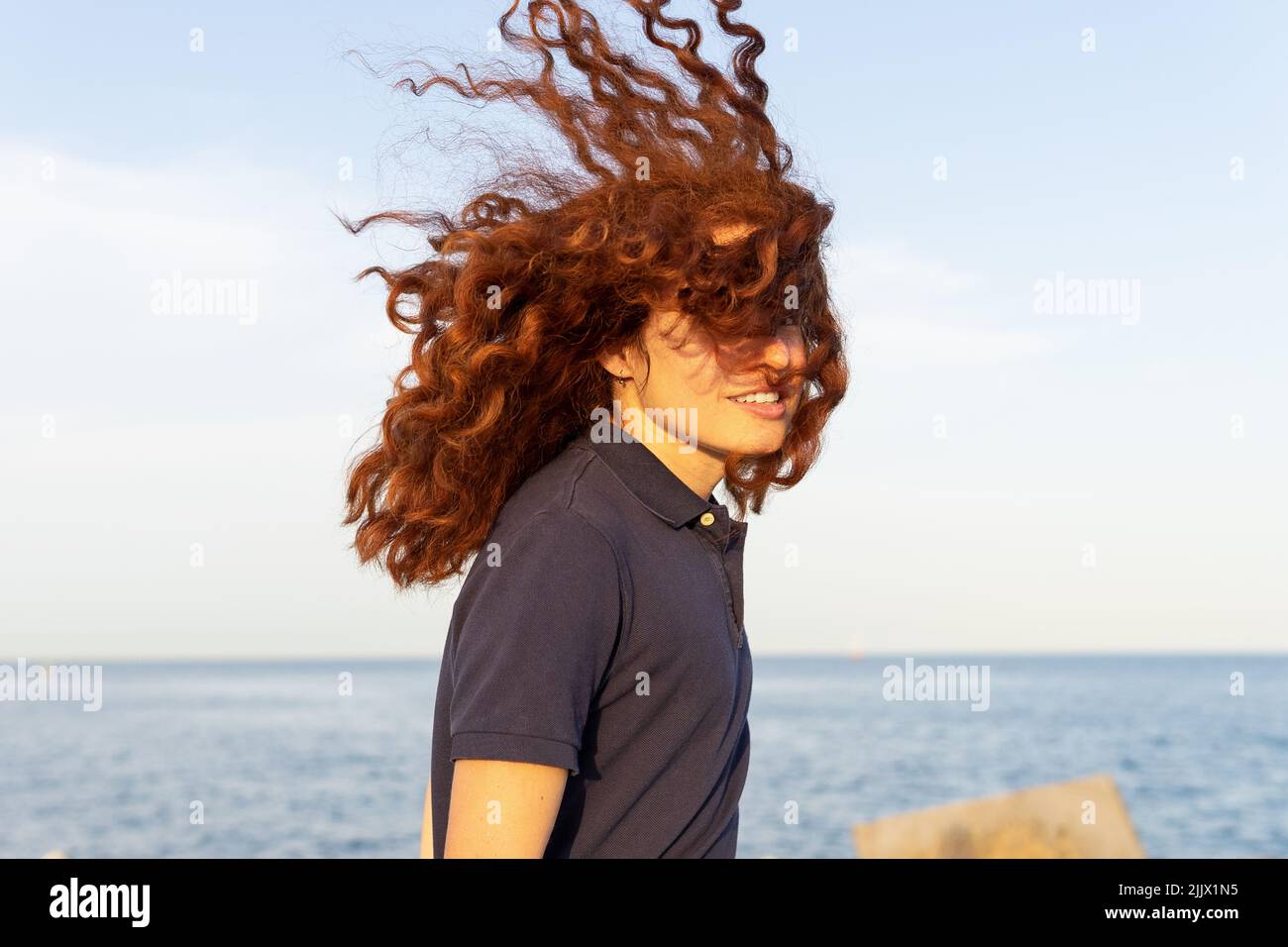 Ritratto di giovane donna allegra con i capelli tousled in piedi alla spiaggia contro il cielo Foto Stock