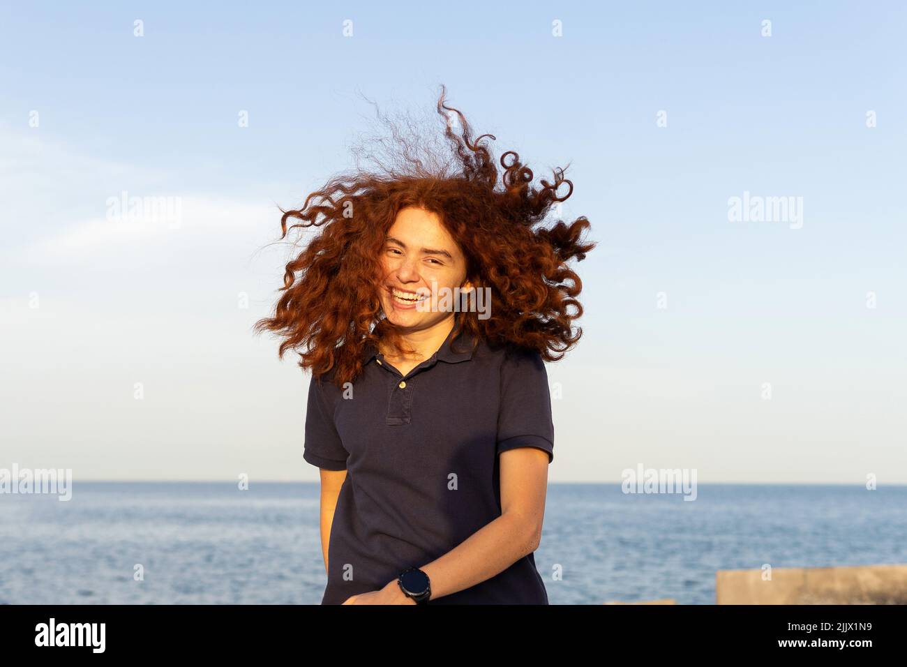 Ritratto di giovane donna allegra con i capelli tousled in piedi alla spiaggia contro il cielo Foto Stock