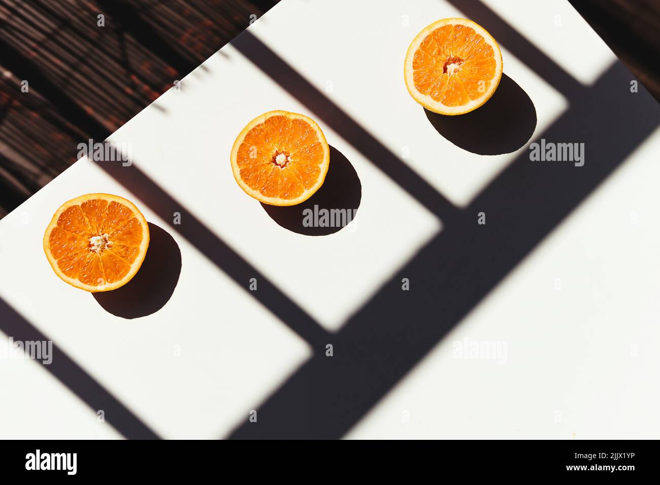 Vista dall'alto delle metà delle arance schiacciate poste su un tavolo bianco vicino all'ombra della ringhiera al mattino soleggiato Foto Stock