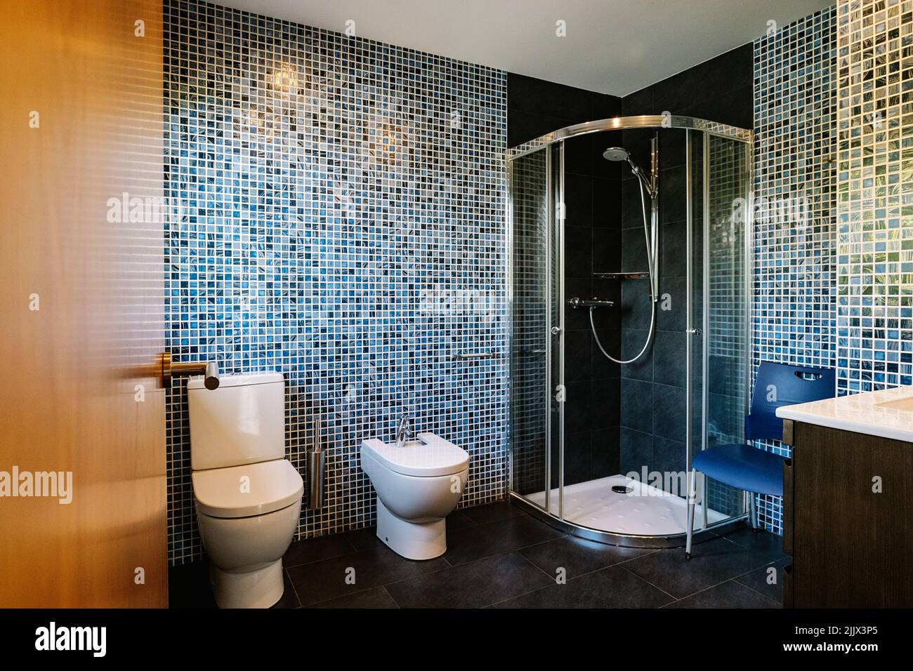 wc in ceramica bianca e bidet vicino alla cabina doccia in bagno moderno con pareti piastrellate in mosaico Foto Stock