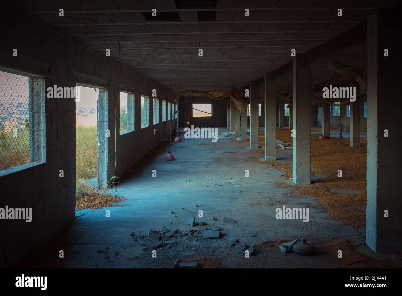 Interno di un edificio industriale desolato scuro con pavimento in shabby e colonne di cemento al tramonto Foto Stock