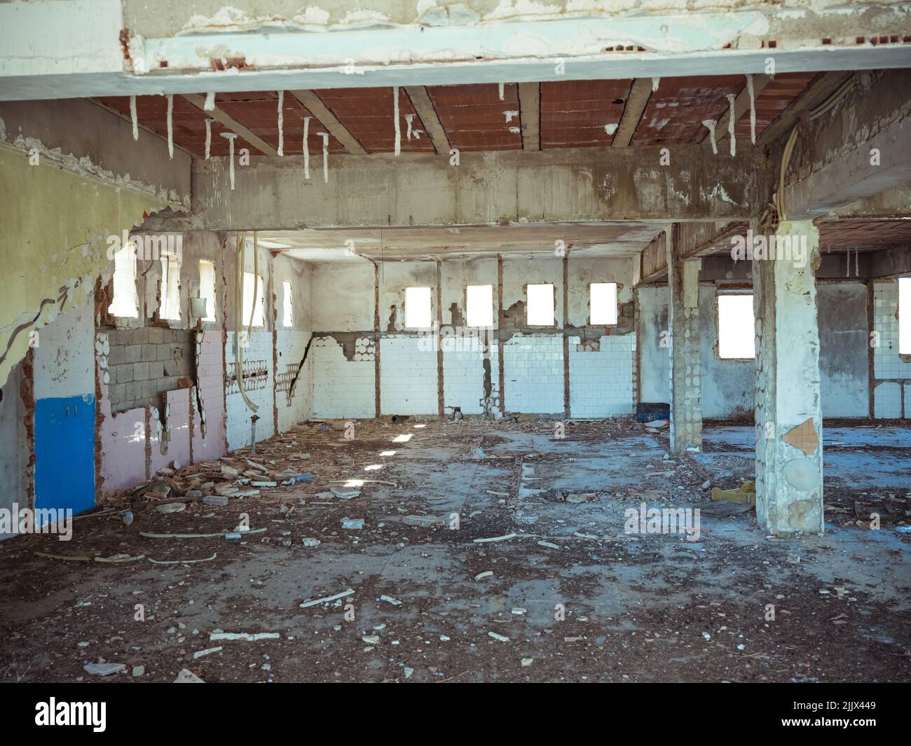 Interno di un edificio industriale desolato scuro con pavimento in shabby e colonne di cemento al tramonto Foto Stock