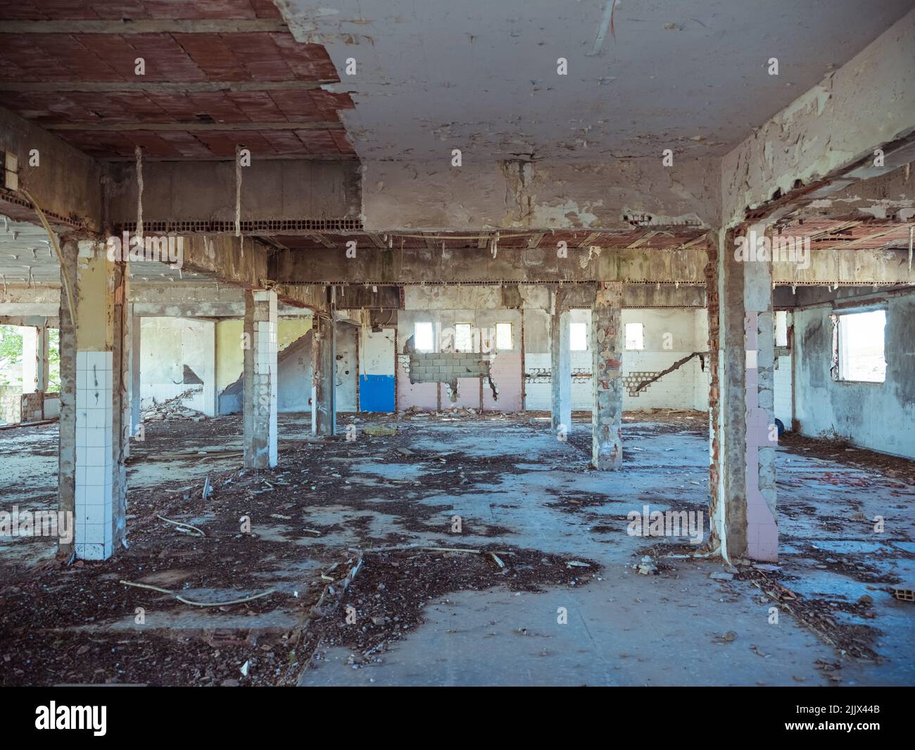 Interno di un edificio industriale desolato scuro con pavimento in shabby e colonne di cemento al tramonto Foto Stock