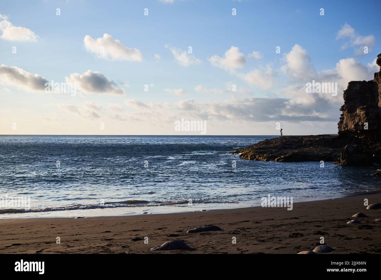 Mare ondinante spiaggia di sabbia con ruvida scogliera rocciosa contro cielo nuvoloso il giorno d'estate nella zona costiera della natura Foto Stock
