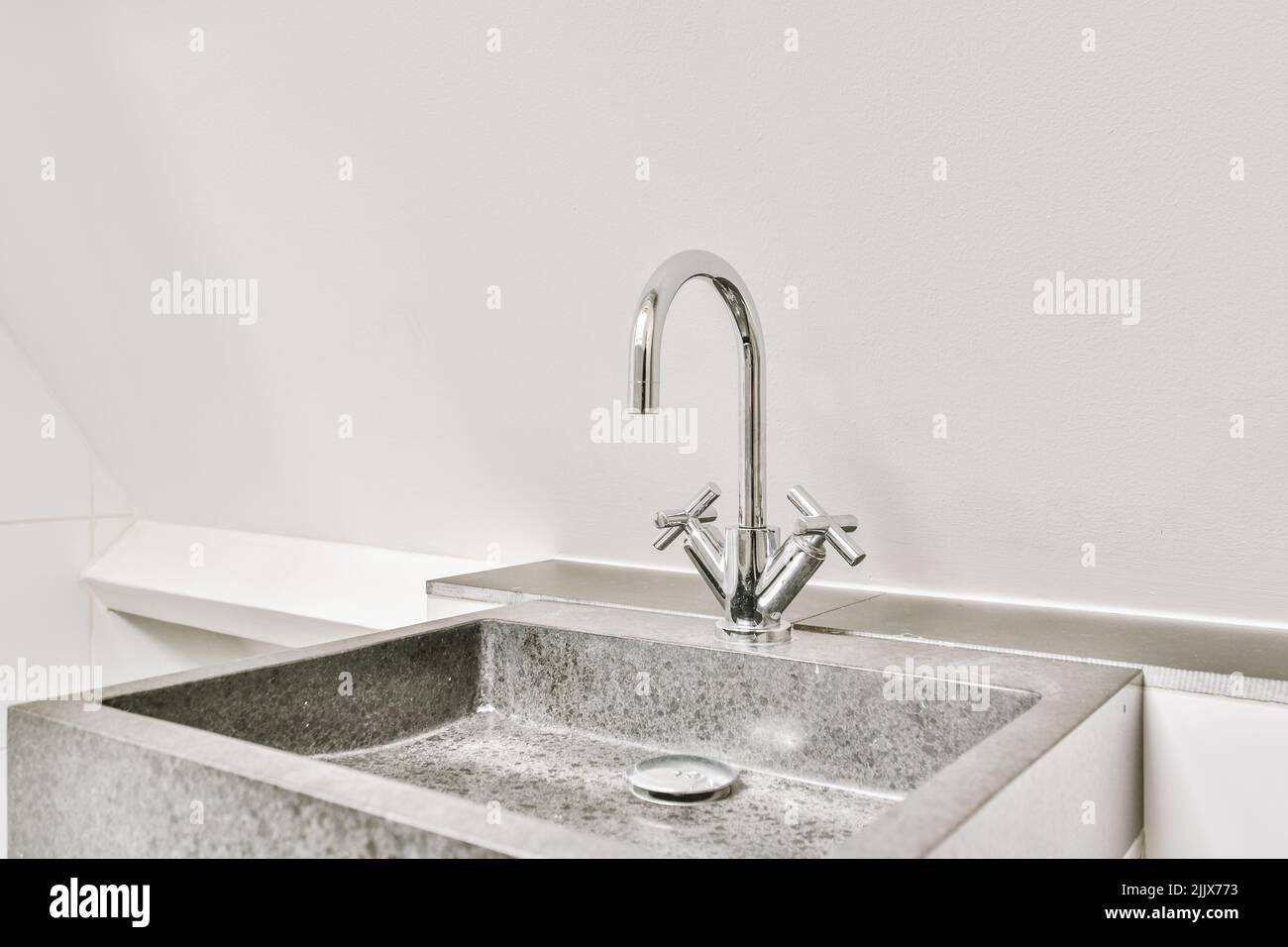 Particolare del lavello con rubinetto in luminoso accanto alla parete bianca Foto Stock