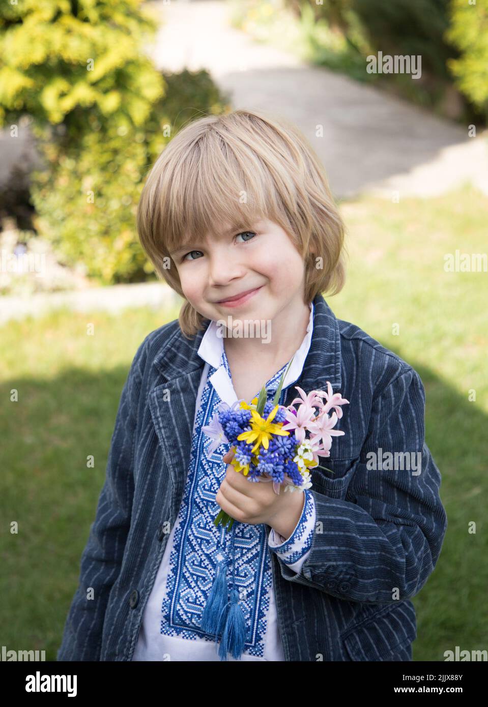 Sorridente ragazzo ucraino di 5 anni in vyshyvanka. Contiene fiori per mamma, guerriero. Orgoglio, libertà, indipendenza, gratitudine. Giorno della vittoria. Pace a Ukrain Foto Stock