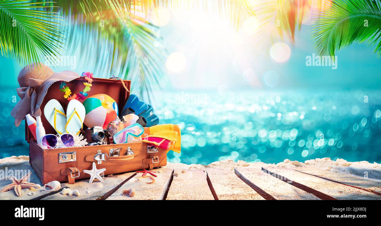 Viaggi Suitcase sulla spiaggia tropicale con il mare soleggiato e le foglie di palma - sfondo astratto sfocato Foto Stock