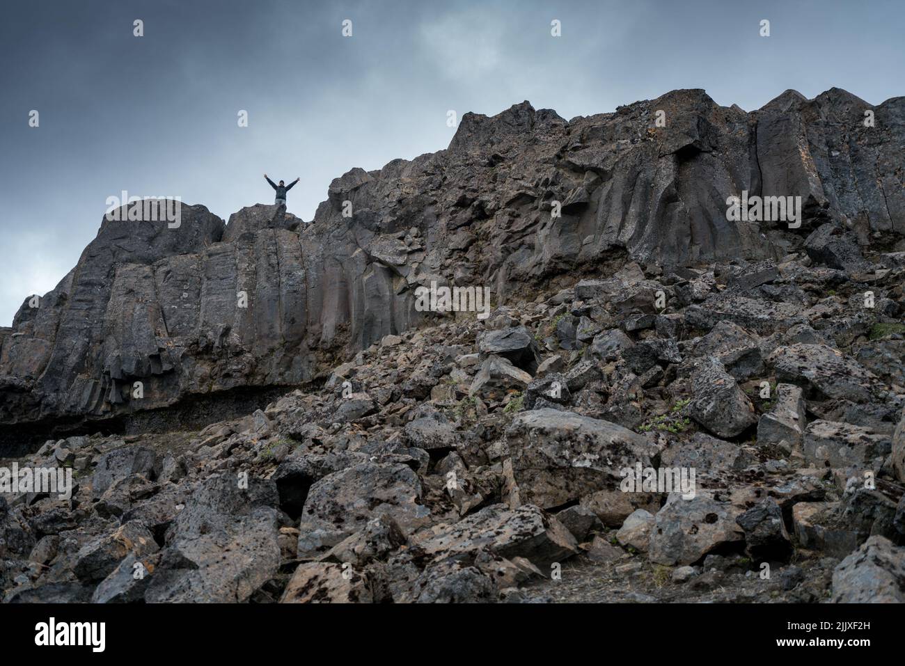 Dettifoss, Islanda - 06.15.2017: Uomo con braccio disteso in piedi su una cima di roccia basaltica nera vicino alla cascata di Dettioss in Islanda. Foto Stock