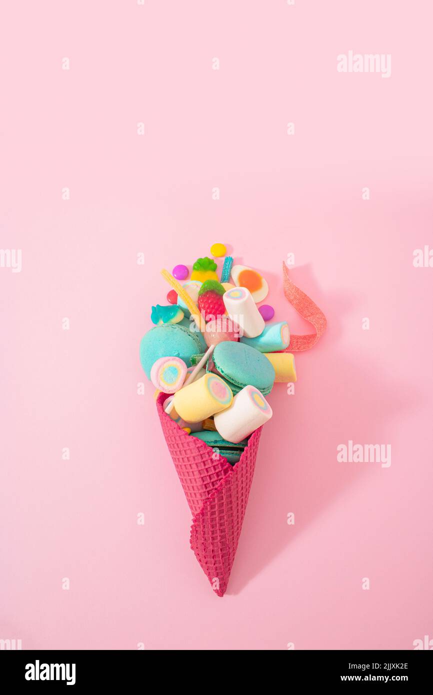 Concetto creativo di cibo spazzatura di un sacco di deliziosi dolci in un cono gelato su sfondo rosa pastello. Bambini, sei in su per un gustoso snack caramella? Foto Stock