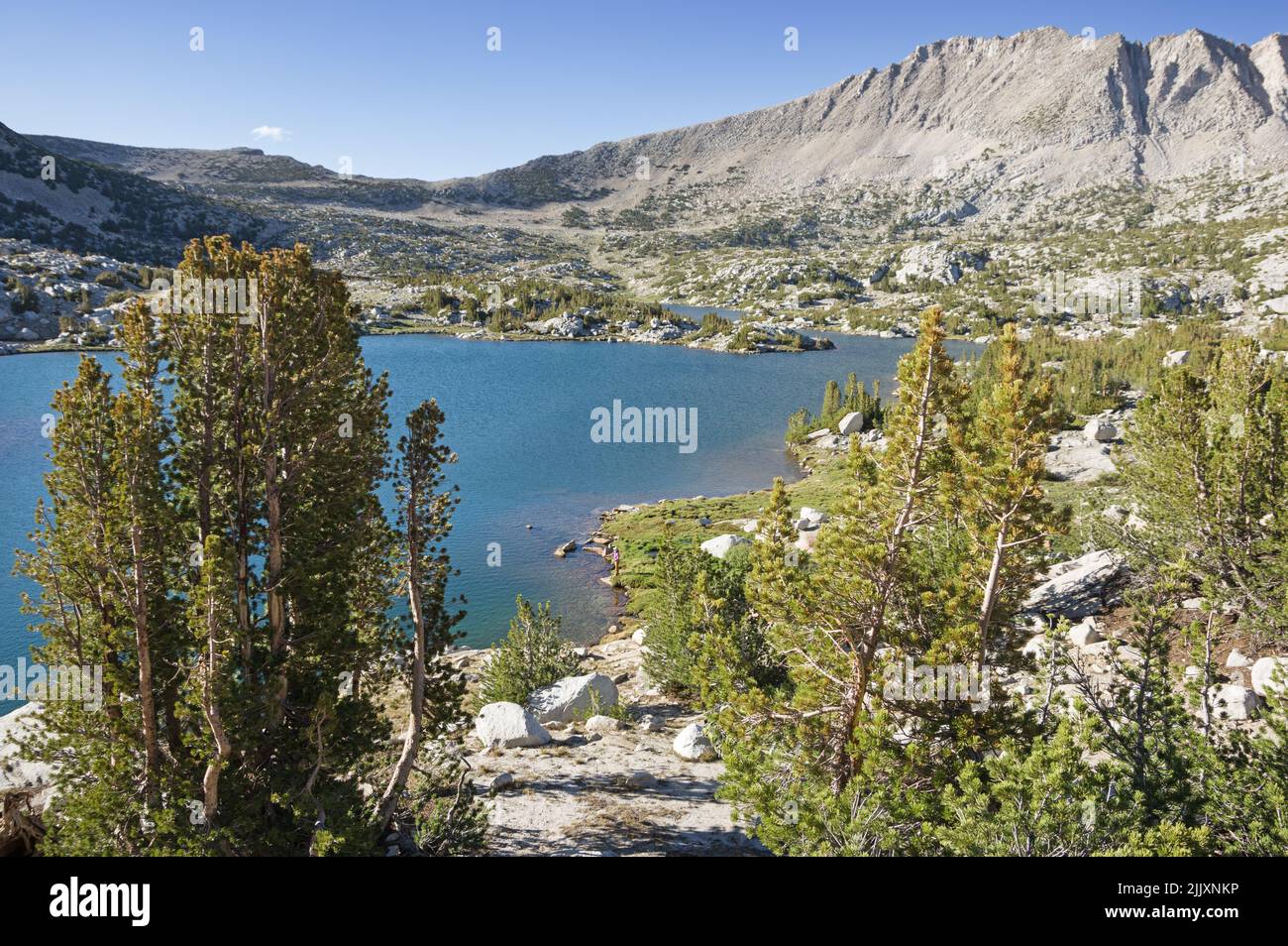 Una vista lontana di una donna che pesca in un lago nel bacino Pioneer, nelle montagne della Sierra Nevada con il monte Stanford North Foto Stock