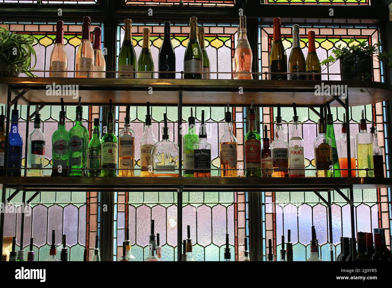 Bottiglie retroilluminate su ripiani in un bar con una vetrata colorata, Regno Unito Foto Stock