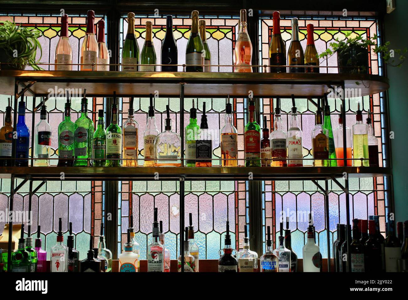 Bottiglie retroilluminate su ripiani in un bar con una vetrata colorata, Regno Unito Foto Stock