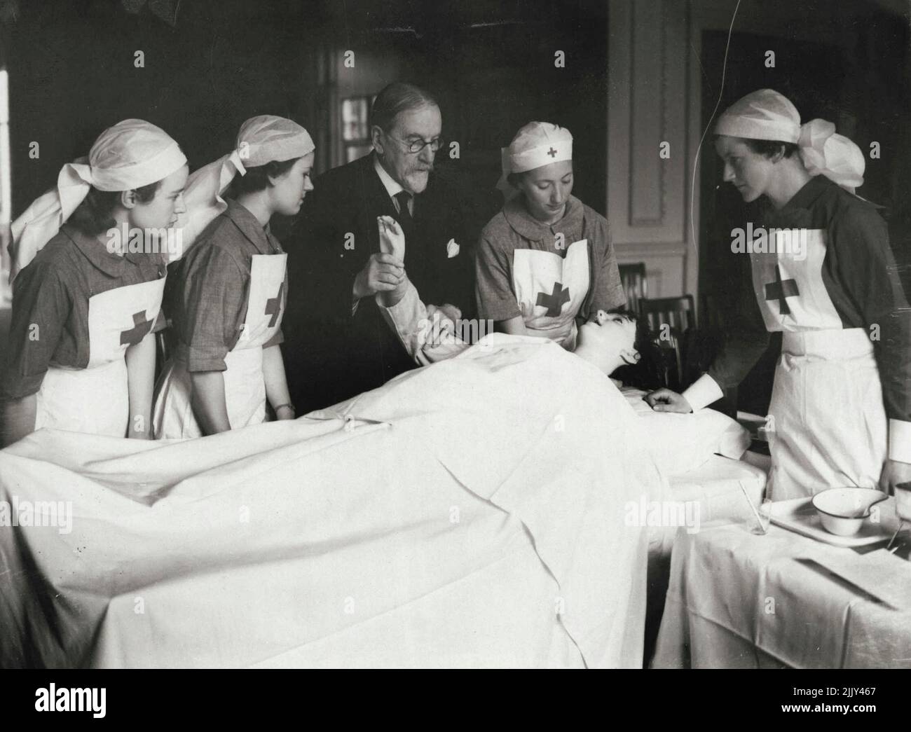 ***** Alla Riserva di Nursing civile ottenga le loro prime lezioni -- i membri della Riserva di Nursing civile nelle loro uniformi blu-grigie astute sono dati l'istruzione pratica da un uomo medico che usa un manichino come 'paziente'. Le reclute si riversano in seguito all'appello per 100.000 infermieri per la Riserva infermieristica civile. Il loro compito in caso di guerra sarà quello di prendersi cura delle vittime e dei bambini evacuati. Le nuove reclute ricevono ora la loro prima istruzione presso la sede della Società della Croce Rossa a Grosvenor Crescent. Aprile 20, 1939. (Foto di Keystone). Foto Stock