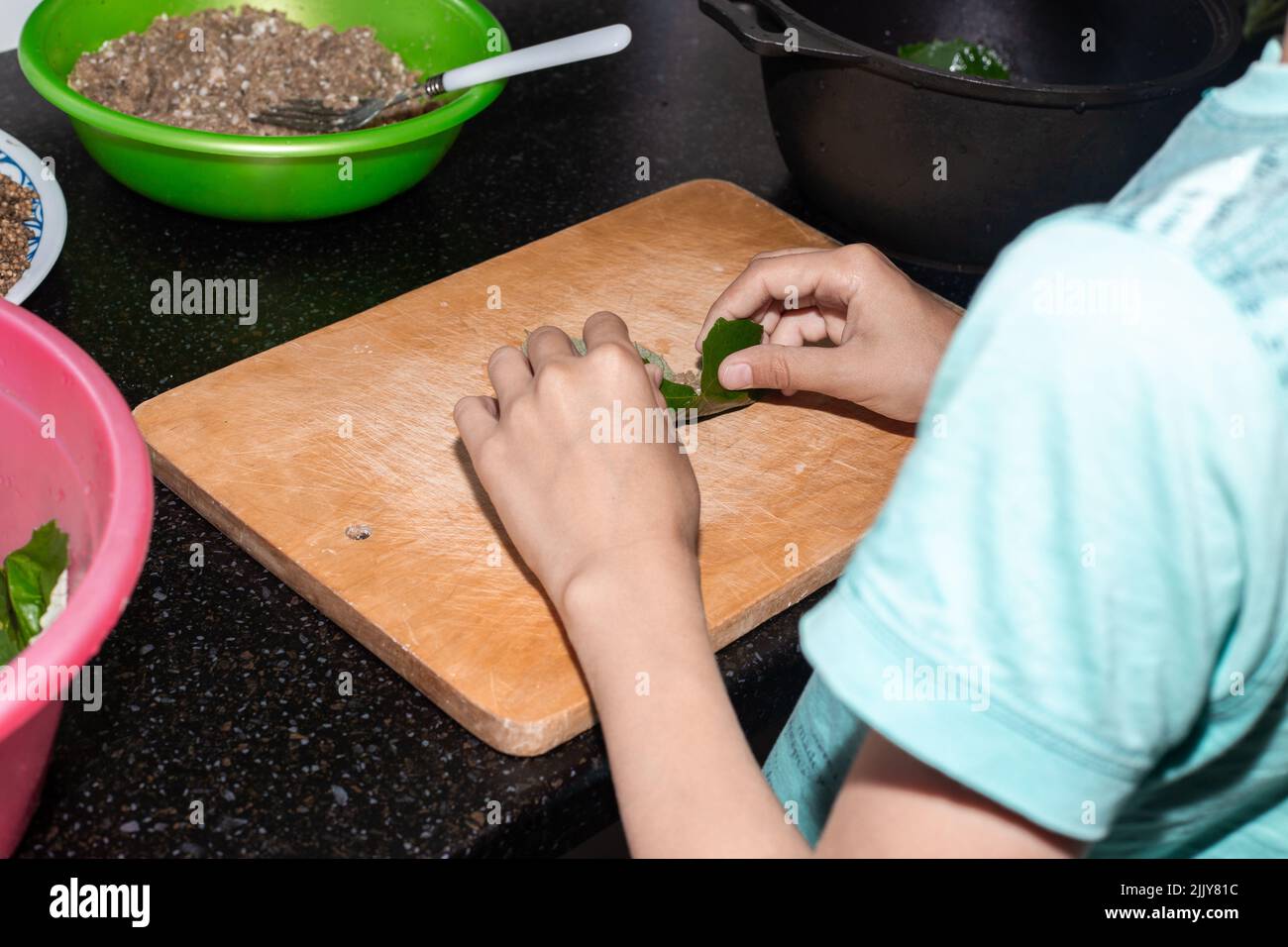 Il ragazzo sta imparando a cucinare. Un bambino avvolge la carne macinata in una foglia d'uva per produrre la dolma. Foto Stock