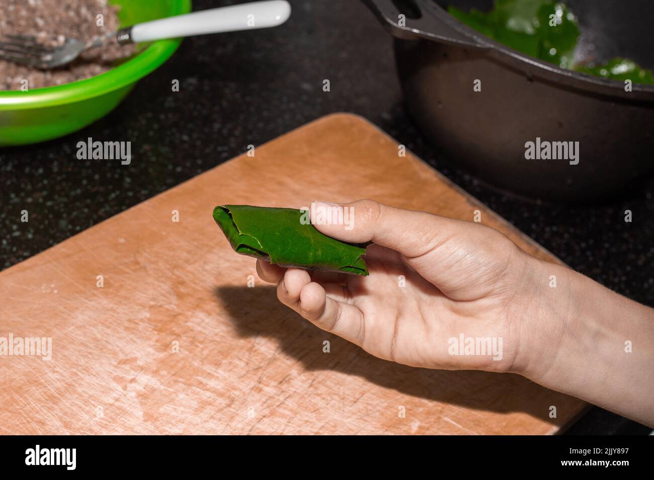 Il ragazzo sta imparando a cucinare. Un bambino affina una foglia d'uva con carne, facendo dolma. Foto Stock