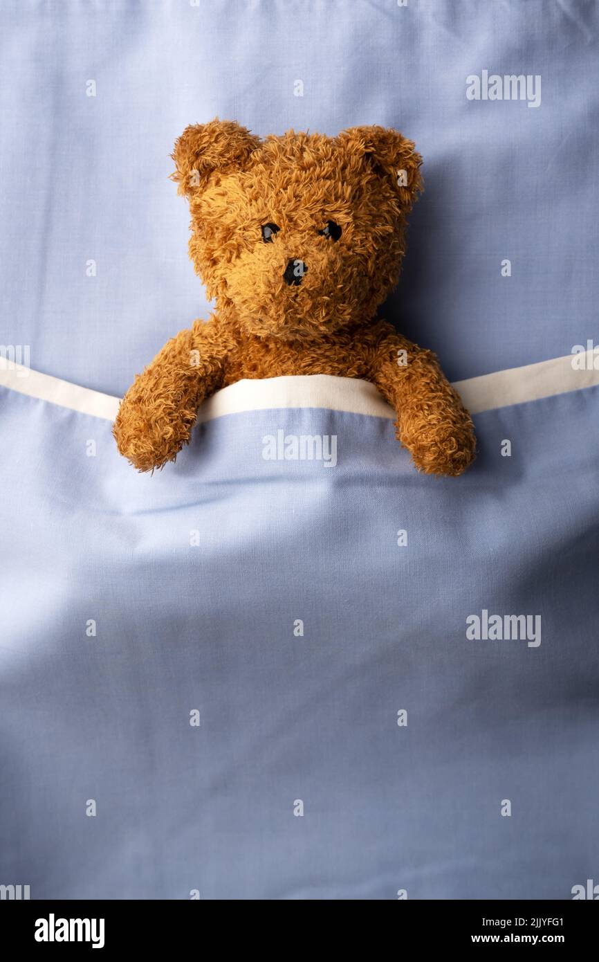Orsacchiotto marrone adagiato sul letto blu. Concetto di medicina pediatrica e infantile Foto Stock