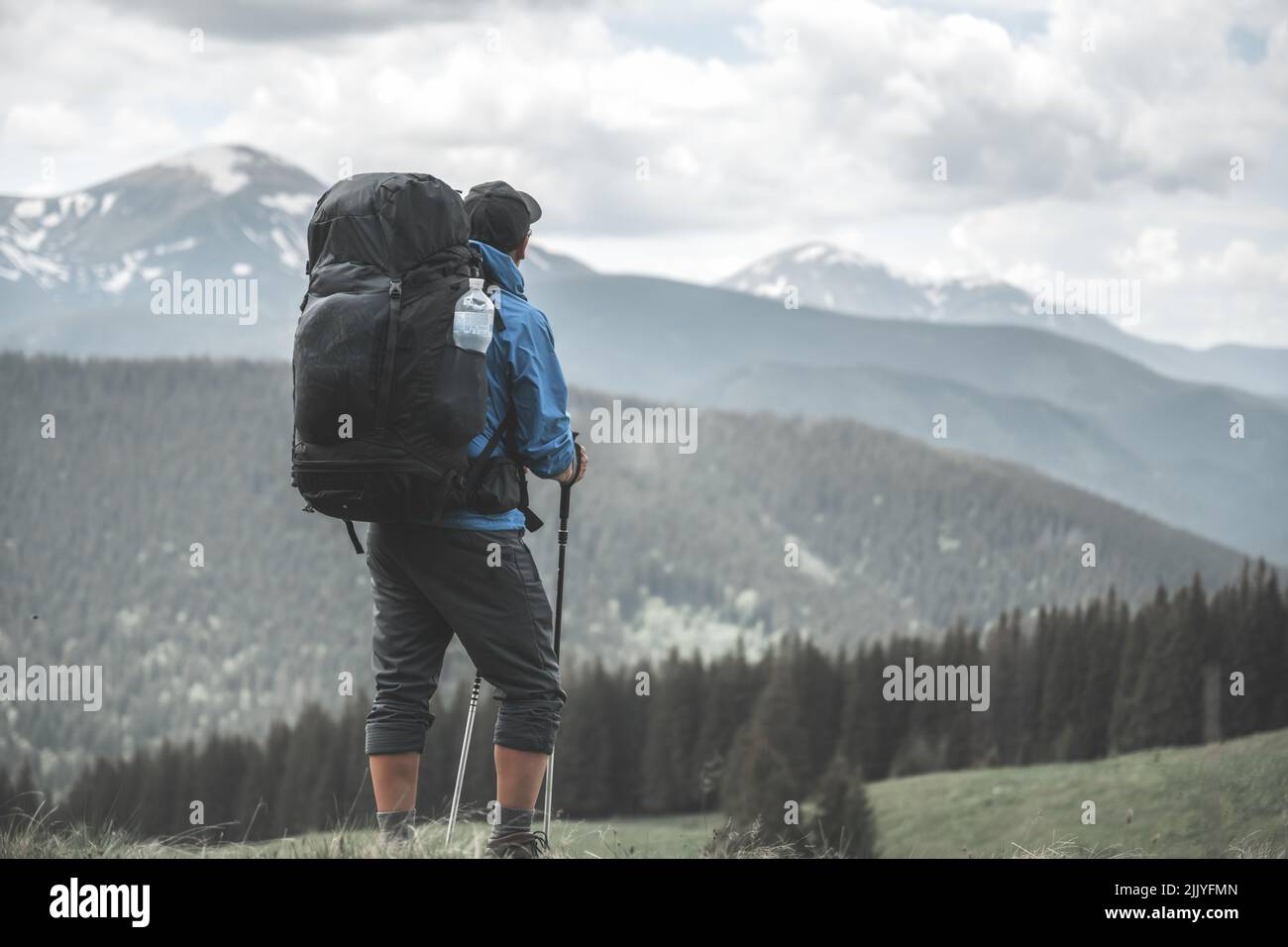 Un turista con zaino escursioni in primavera montagne. Montagne innevate sullo sfondo. Fotografia di paesaggio Foto Stock