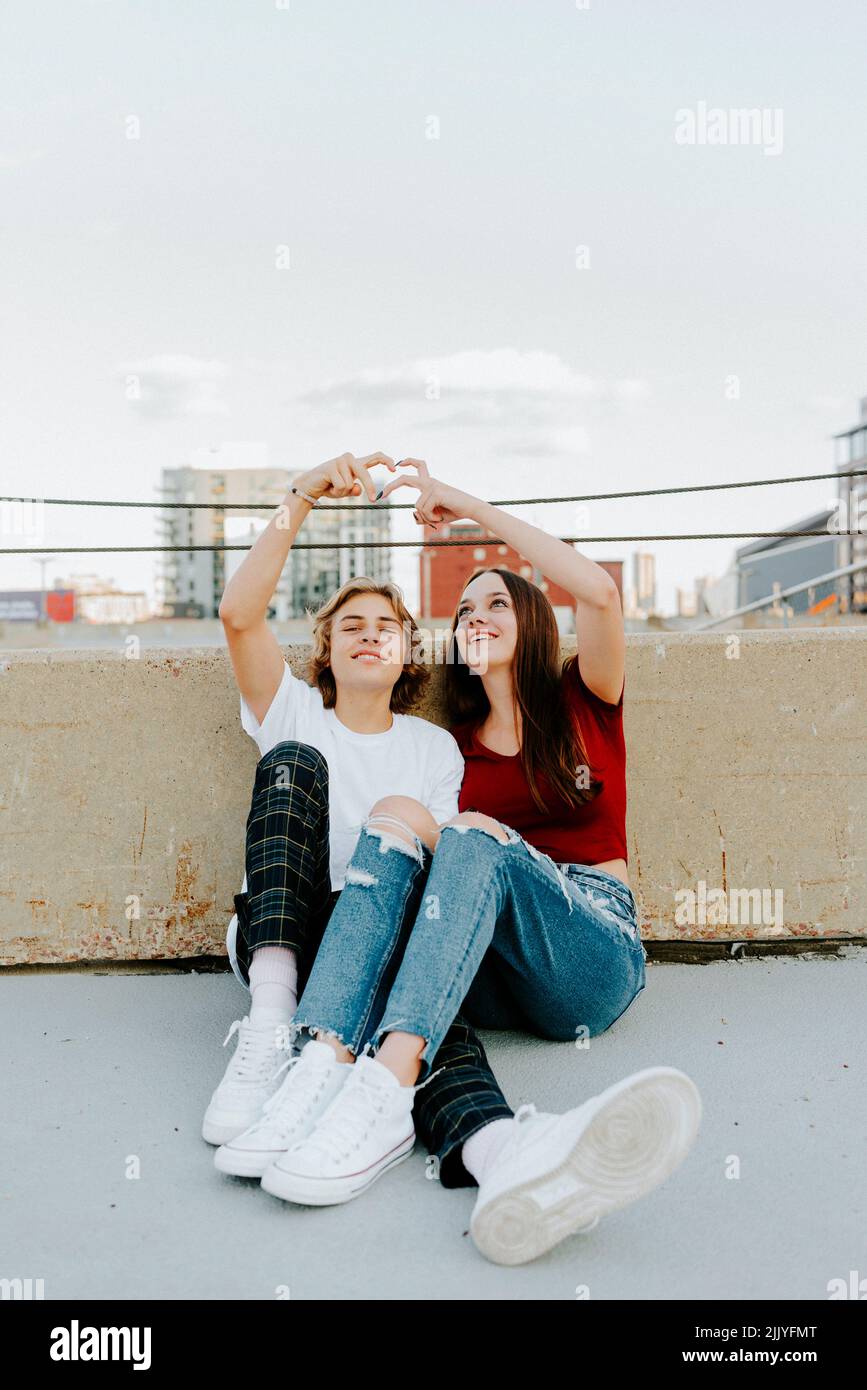 fidanzata e ragazza seduta sul tetto che fa simbolo del cuore Foto Stock