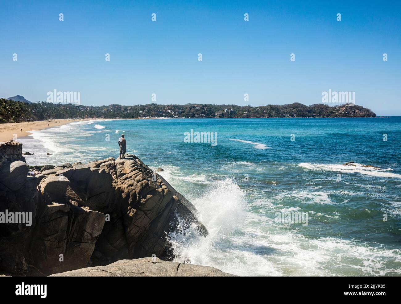 Onde che si infrangono sulle rocce all'estremità nord di Playa Sayulita con un uomo in piedi sulle rocce, Sayulita, Nayarit, Messico. Foto Stock