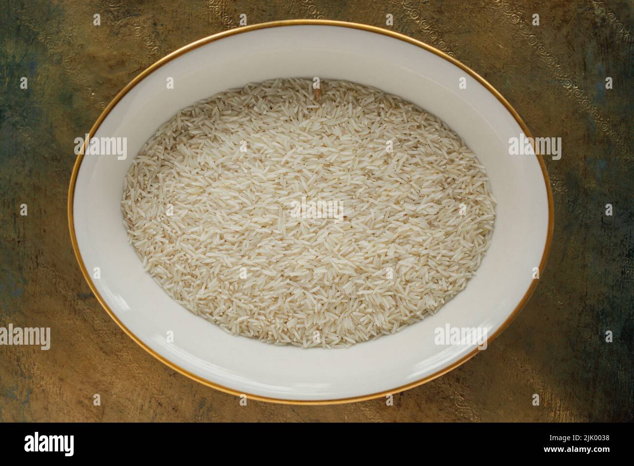 Grani di riso Basmati secchi e crudi in piatto su superficie dorata Foto Stock