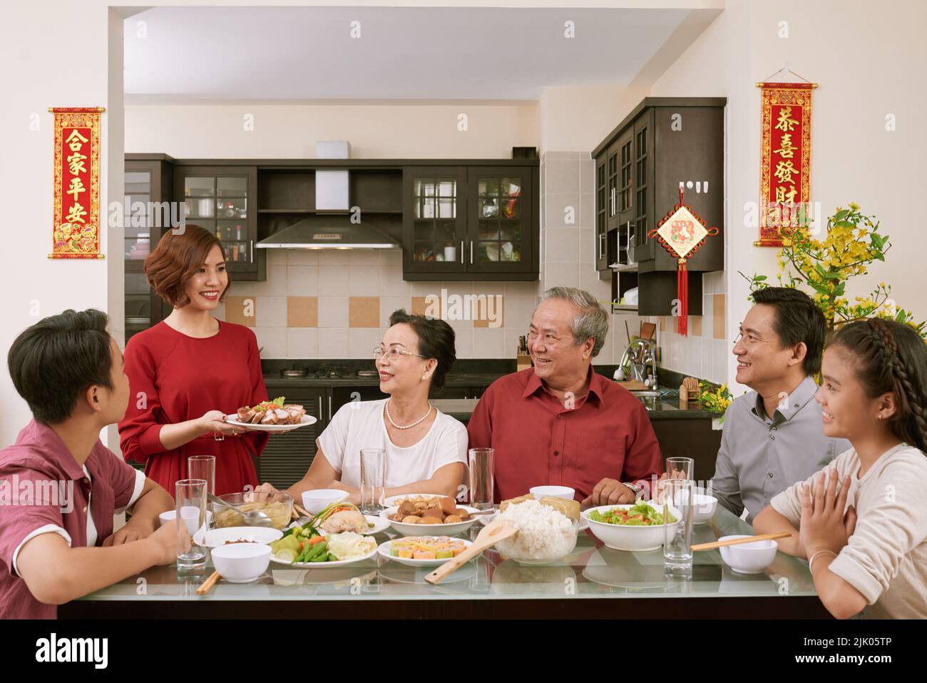 Donna sorridente che porta il piatto principale alla cena di famiglia Tet. Scorre desiderio di fortuna e ricchezza in background Foto Stock