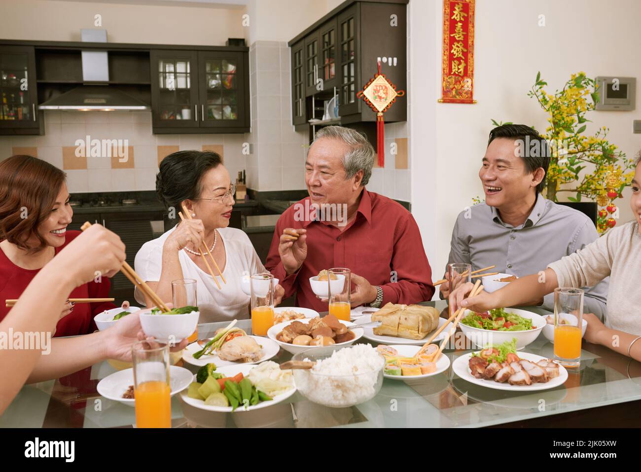 La famiglia si diverse a parlare e a gustare del buon cibo durante la celebrazione del Capodanno cinese. Scorre desiderio di fortuna e ricchezza in background Foto Stock