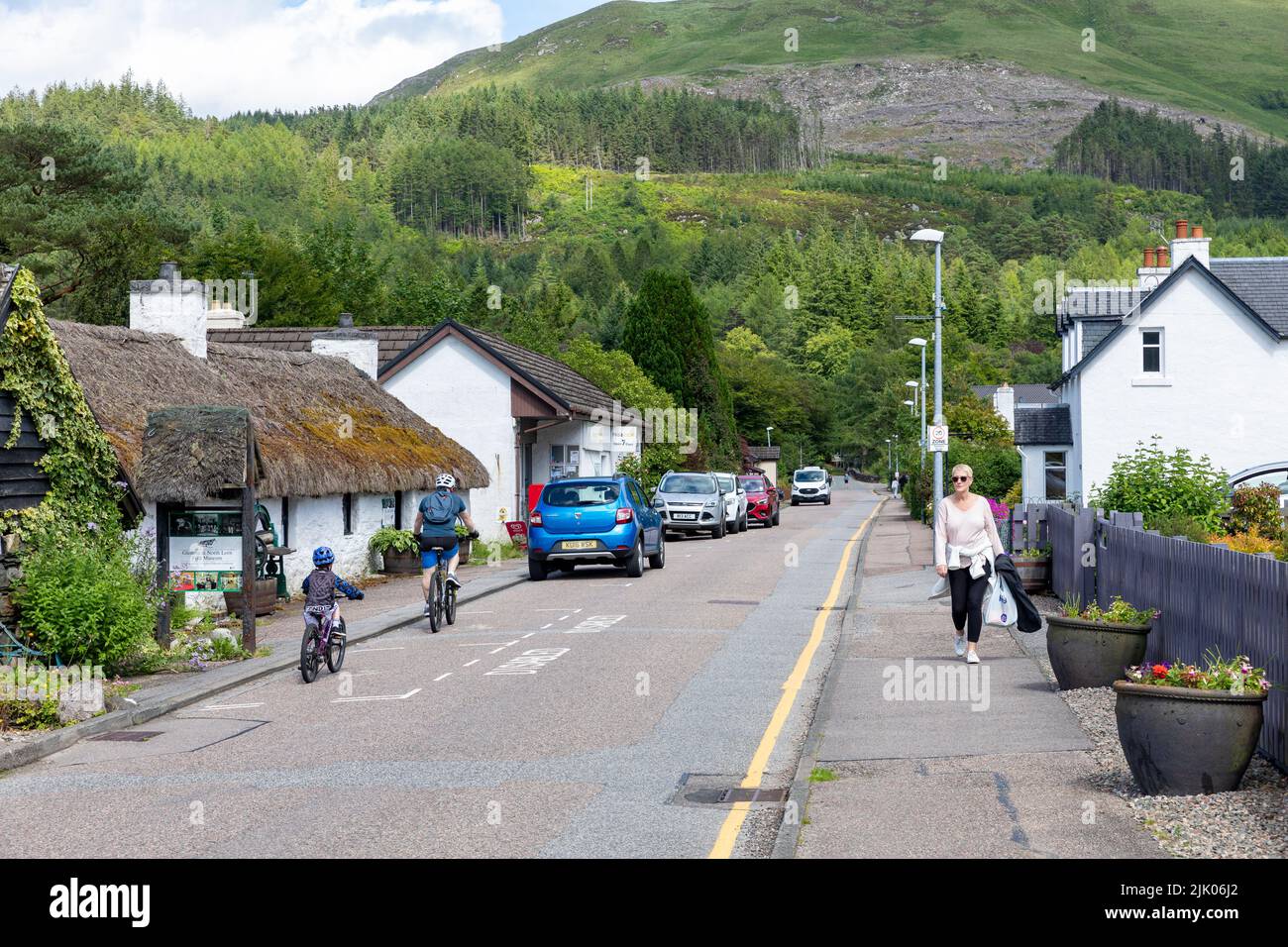Glencoe villaggio con negozi e case, Highlands scozzesi, Scozia in una giornata estiva, padre e figlio in bicicletta, Regno Unito Foto Stock