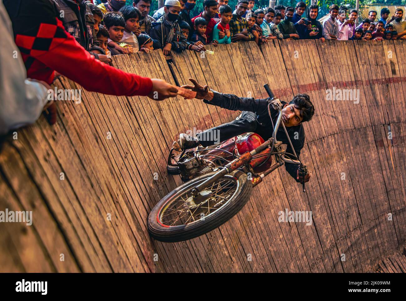 I motociclisti temerari girano intorno a un ripido "muro della morte" a 50 miglia all'ora con un pilone dietro Foto Stock