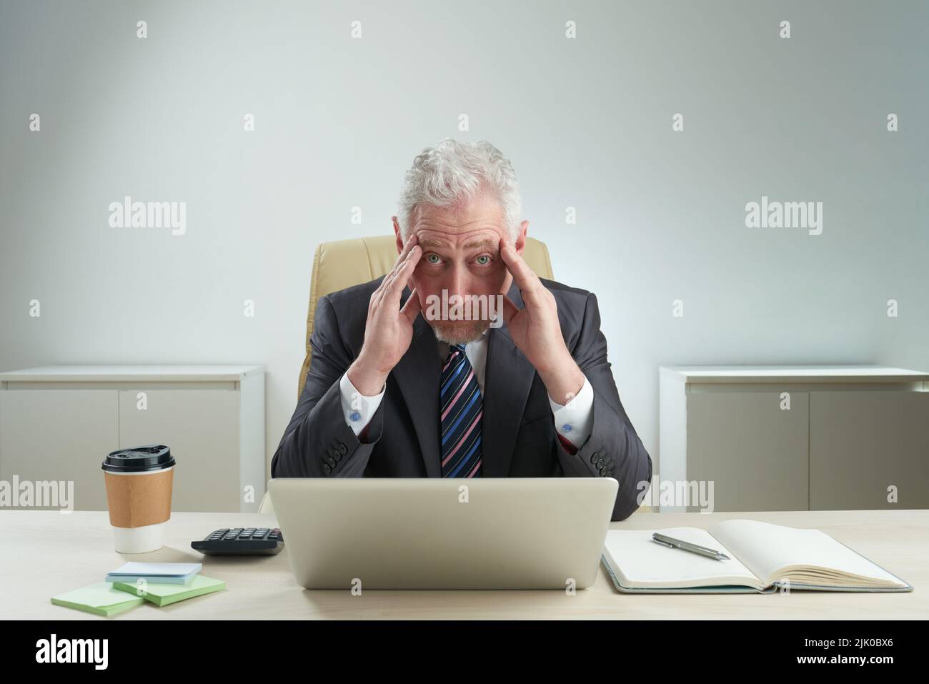 Stanco lavoratore colletto bianco anziano che guarda la macchina fotografica mentre sfrega le sue stanghette e seduto alla scrivania d'ufficio, ritratto giretto vita-su Foto Stock
