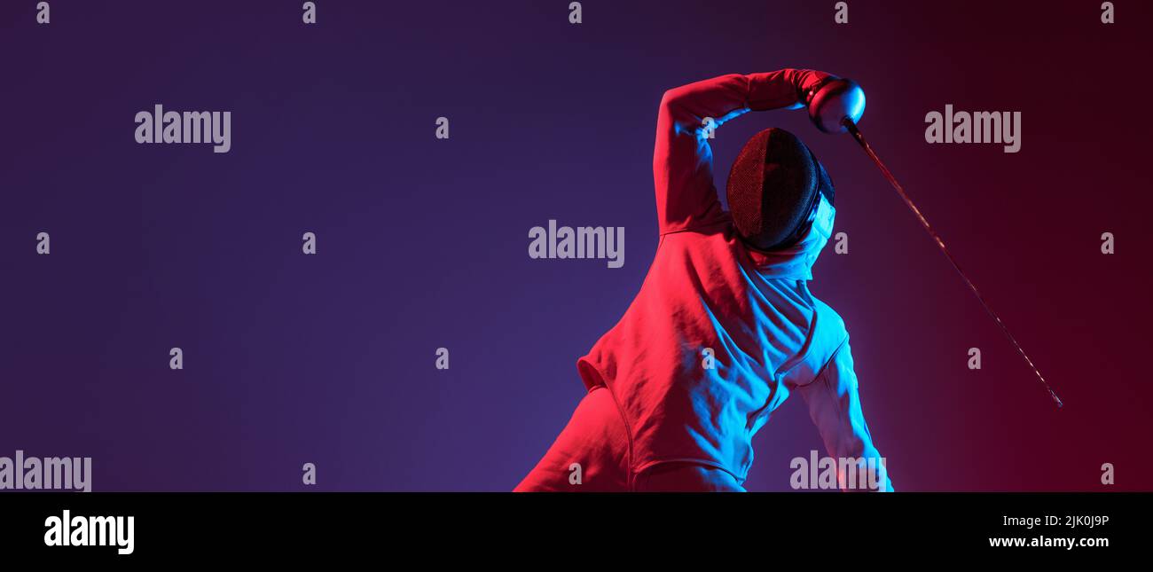 Fencer maschio con spada piccola pratica scherma isolato su sfondo viola in luce al neon. Sport, energia, abilità, realizzazioni Foto Stock