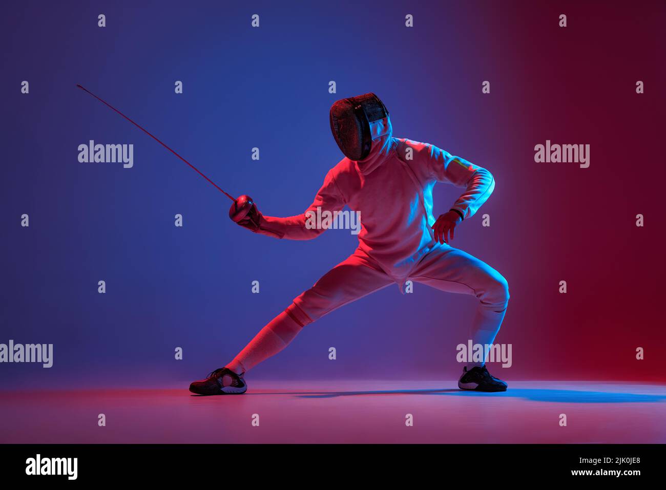 Fencer maschio con spada piccola pratica scherma isolato su sfondo viola in luce al neon. Sport, energia, abilità, realizzazioni Foto Stock