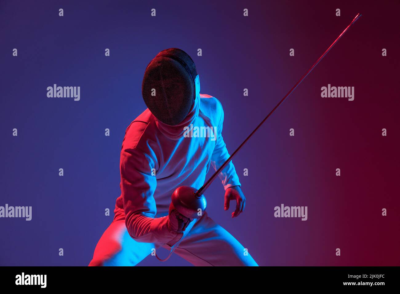 Fencer maschio con spada piccola pratica scherma isolato su sfondo viola in luce al neon. Sport, energia, abilità, realizzazioni Foto Stock
