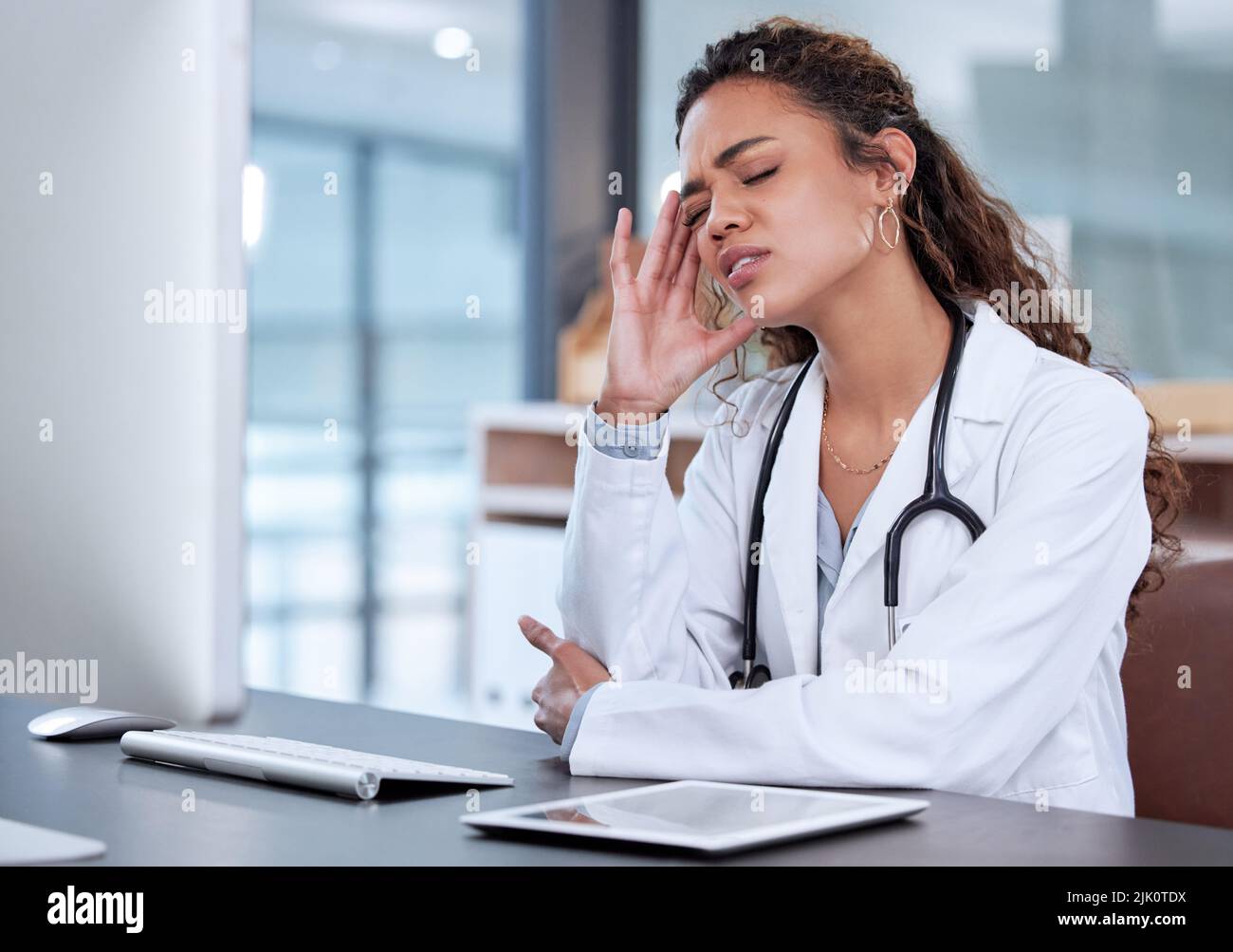 Burnout può causare problemi fisici. Una giovane dottore femminile che soffre di mal di testa sul lavoro. Foto Stock