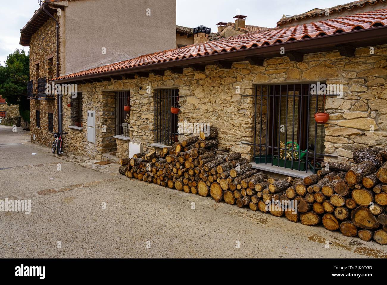 Legna da ardere accatastata sulla facciata di una vecchia casa in pietra e bicicletta parcheggiata all'ingresso. Madrid. Foto Stock
