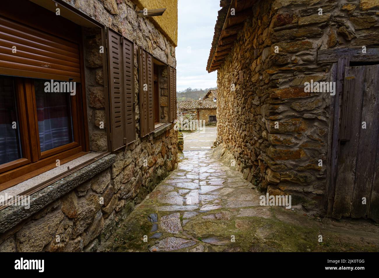 Vicolo stretto tra case in pietra con luce sullo sfondo e riflessi sul terreno bagnato dalla pioggia. Spagna. Foto Stock