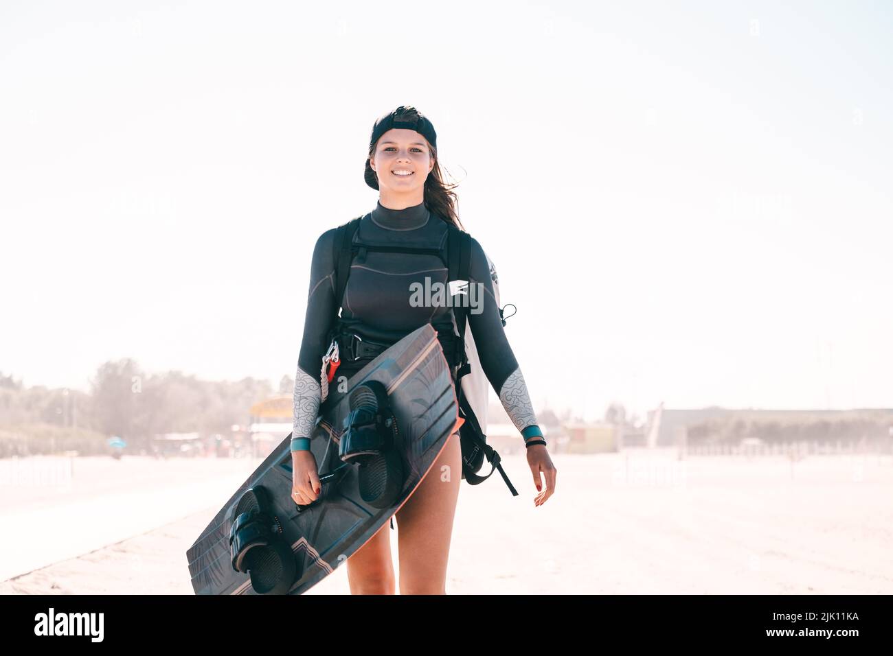 Ritratto di bella ragazza sorridente in posa con una tavola da surf sulla spiaggia e indossare kitesurf attrezzatura - concetto di donna sportiva e sport estivo Foto Stock