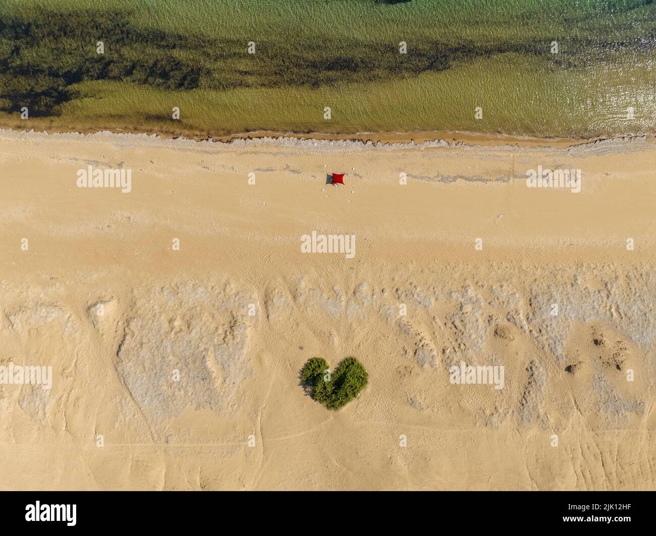Veduta aerea della spiaggia di Paralia Issos a Corfù, Grecia. Tenda. Tenda da spiaggia. Bagnanti. Bush a forma di cuore in mezzo alla sabbia. Ama la spiaggia. Foto Stock