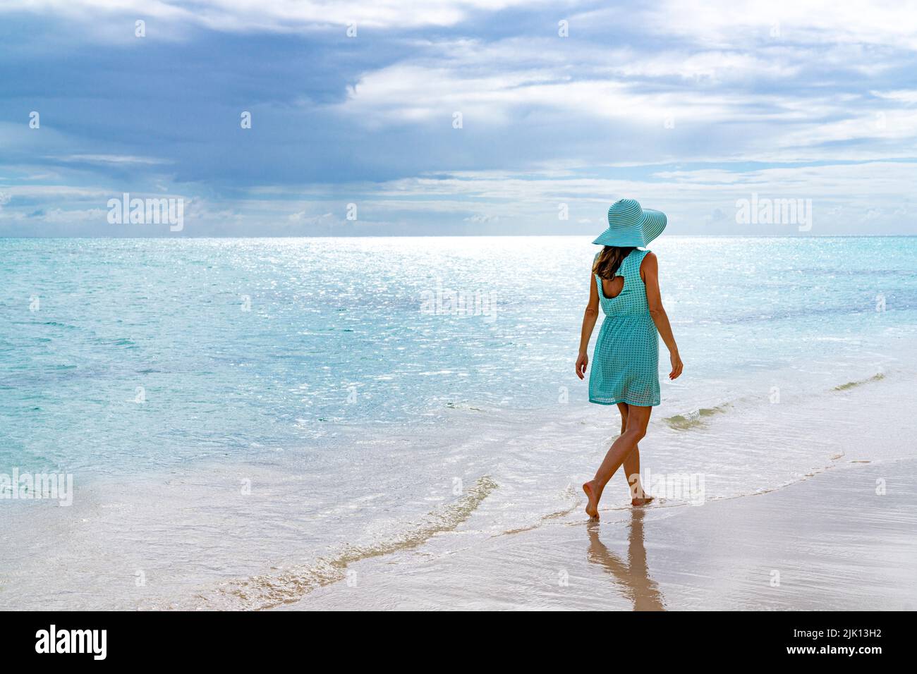 Donna che cammina su una spiaggia di sabbia bianca sotto il cielo nuvoloso al tramonto, Barbuda, Antigua e Barbuda, Indie Occidentali, Caraibi, America Centrale Foto Stock