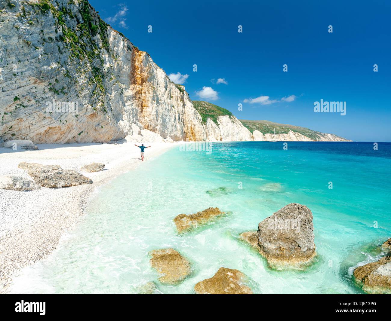 Vista aerea di un uomo allegro con le braccia distese ammirando il mare cristallino a Fteri Beach, Cefalonia, Isole IONIE, Isole Greche, Grecia, Europa Foto Stock