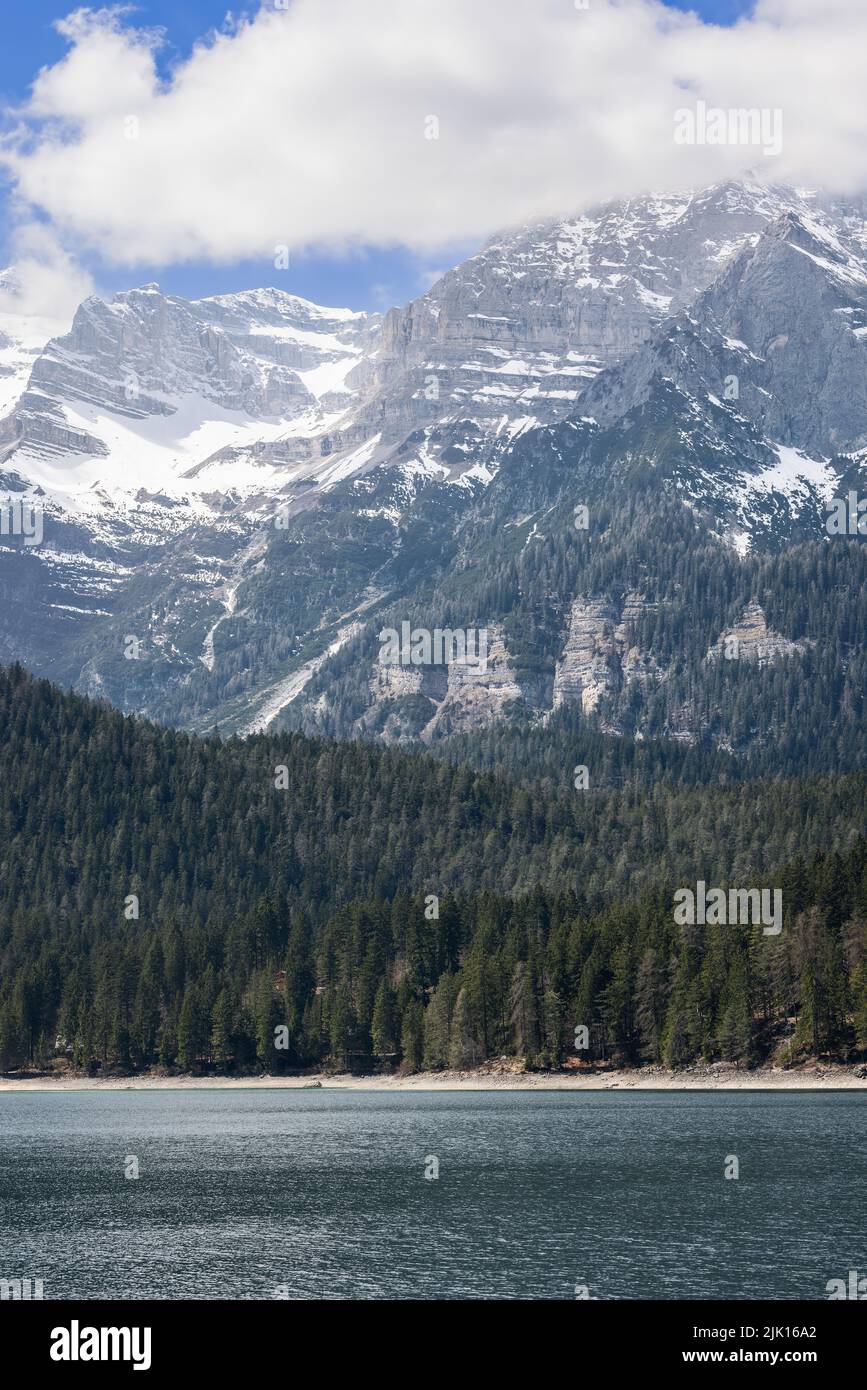 Colpo verticale di lago alpino Tovel e scogliere con tracciati geologici tracciabili ricoperti di verde foresta e neve, Trentino, Italia Foto Stock