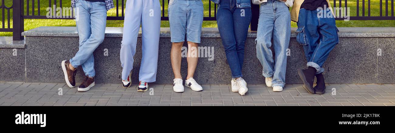 Gambe di sei giovani in eleganti abiti in denim in fila sulla strada della città. Foto Stock