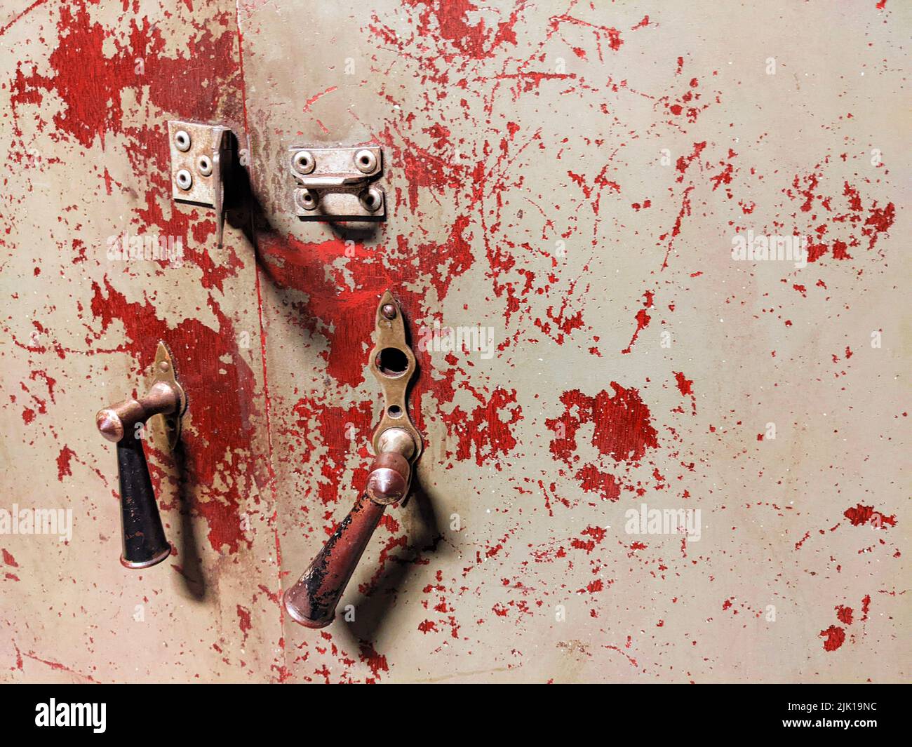 Una vecchia porta usurata con maniglie rotte e tracce di vernice rossa che assomiglia al sangue Foto Stock