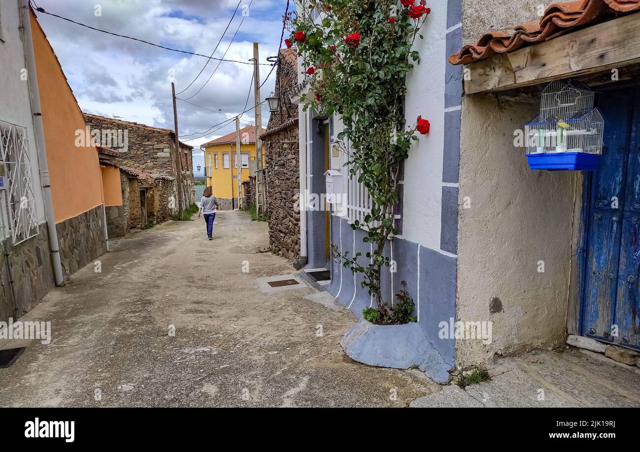 Donna che cammina lungo una strada stretta in una città vecchia con una gabbia di uccelli sulla porta di una casa. Avila Foto Stock