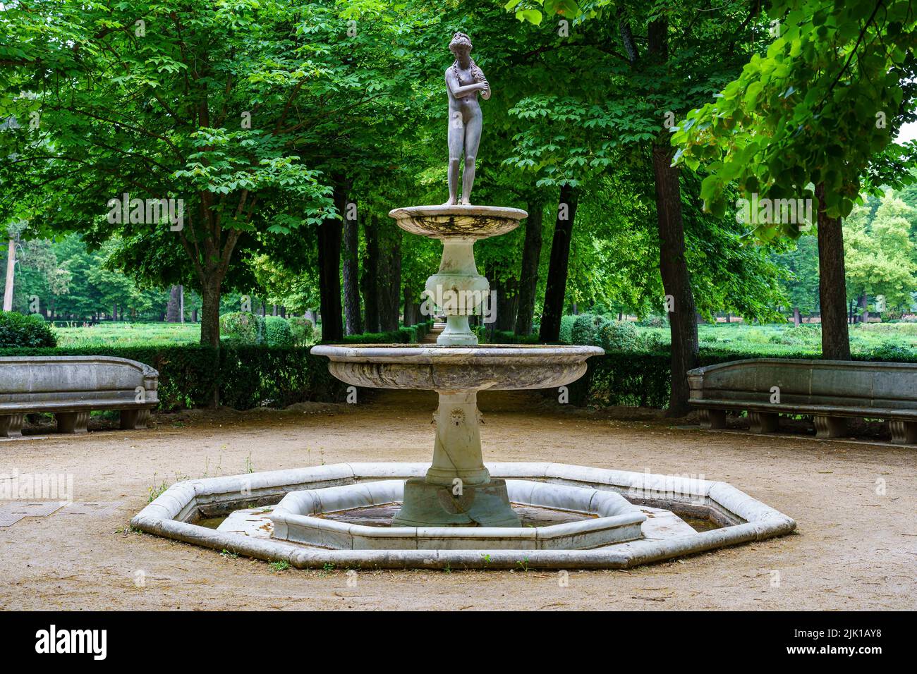 Fontana in pietra bianca con statua nel parco pubblico con vegetazione verde. Foto Stock