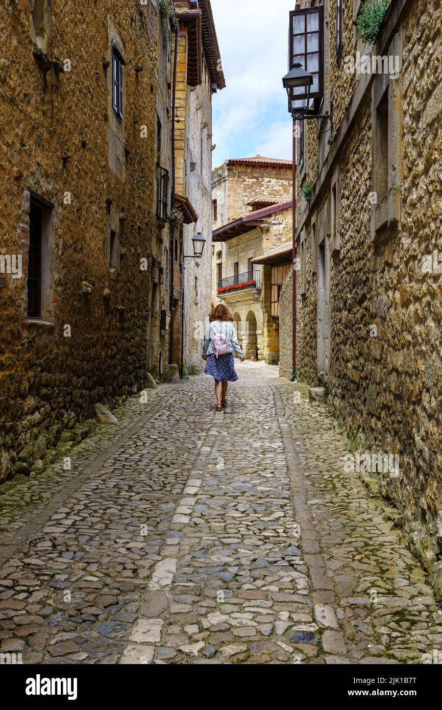 Donna da dietro camminando attraverso un vicolo stretto con vecchie case di pietra. Santilla del Mar, Santander. Foto Stock