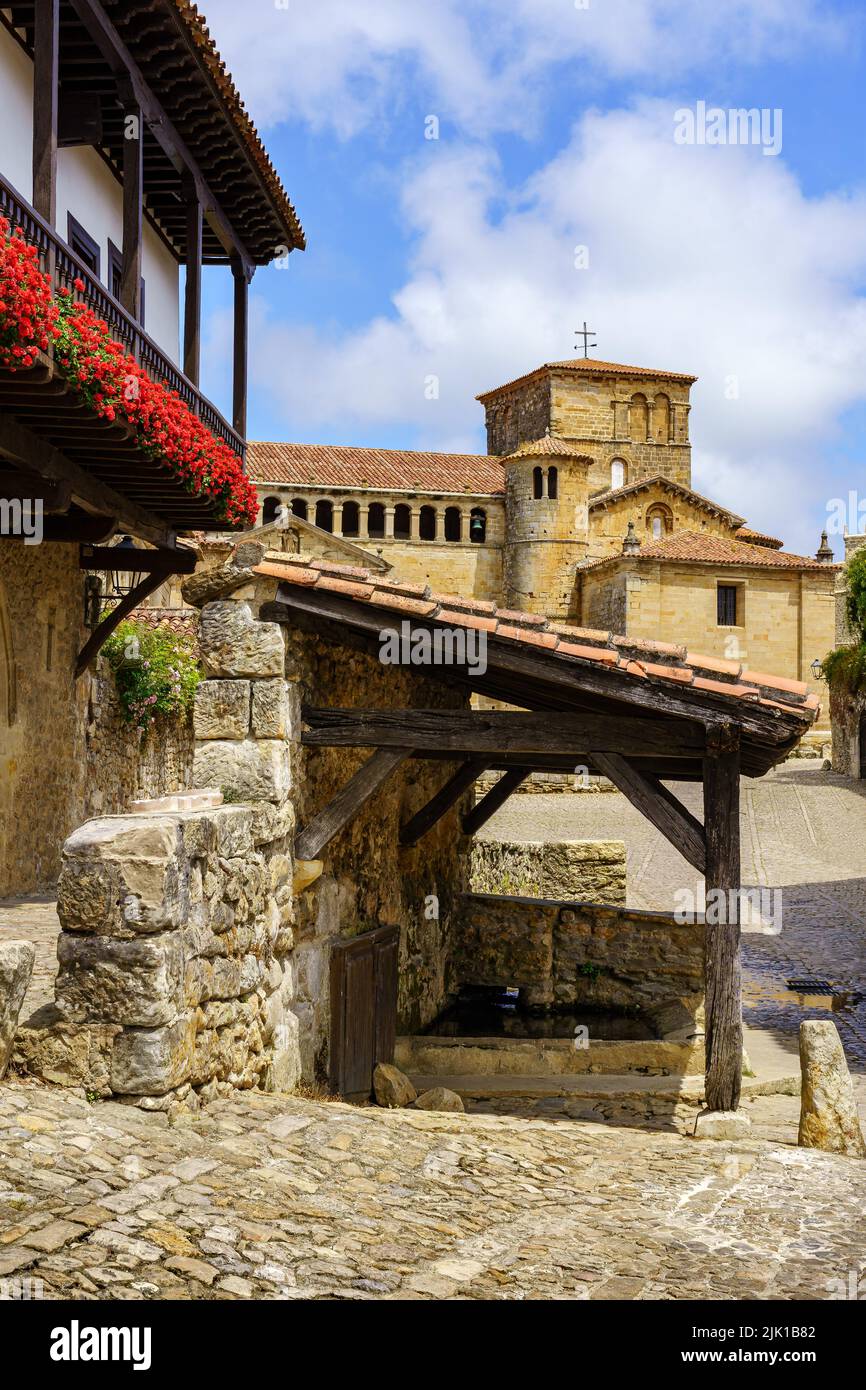 Fontana d'acqua con tetto e chiesa sullo sfondo in un antico borgo medievale. Santillana del Mar, Santander. Foto Stock