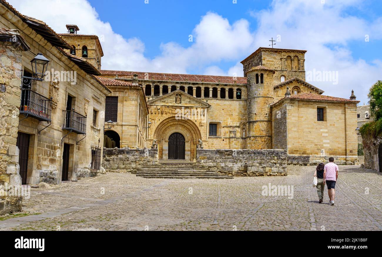 Coppia di persone che camminano in una vecchia città di pietra con una chiesa romanica a Santillana del Mar. Foto Stock