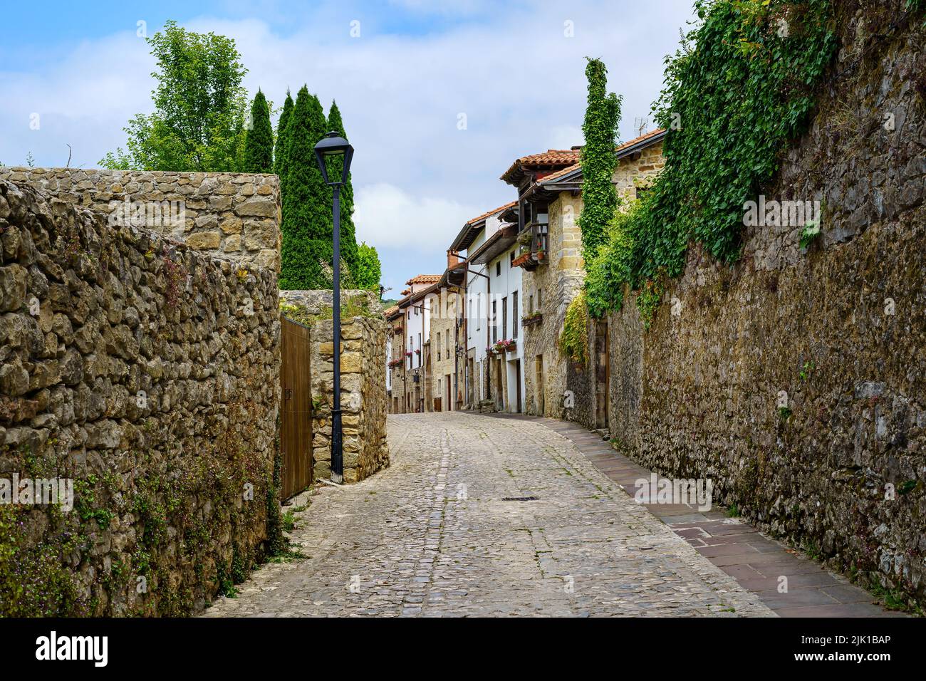Vecchia strada villaggio in pietra con pareti coperte di verde e fiori. Santillana del Mar, Spagna. Foto Stock